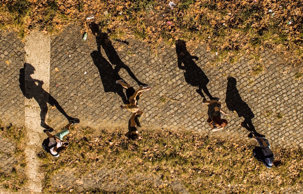 Overhead view of people enjoying a sunny day in the city park, with long shadows.