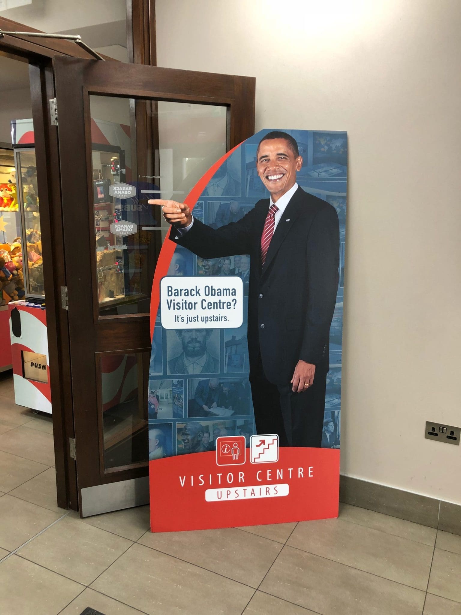 Barack Obama Visitor Centre sign pointing upstairs. Text: "Barack Obama Visitor Centre? It's just upstairs.