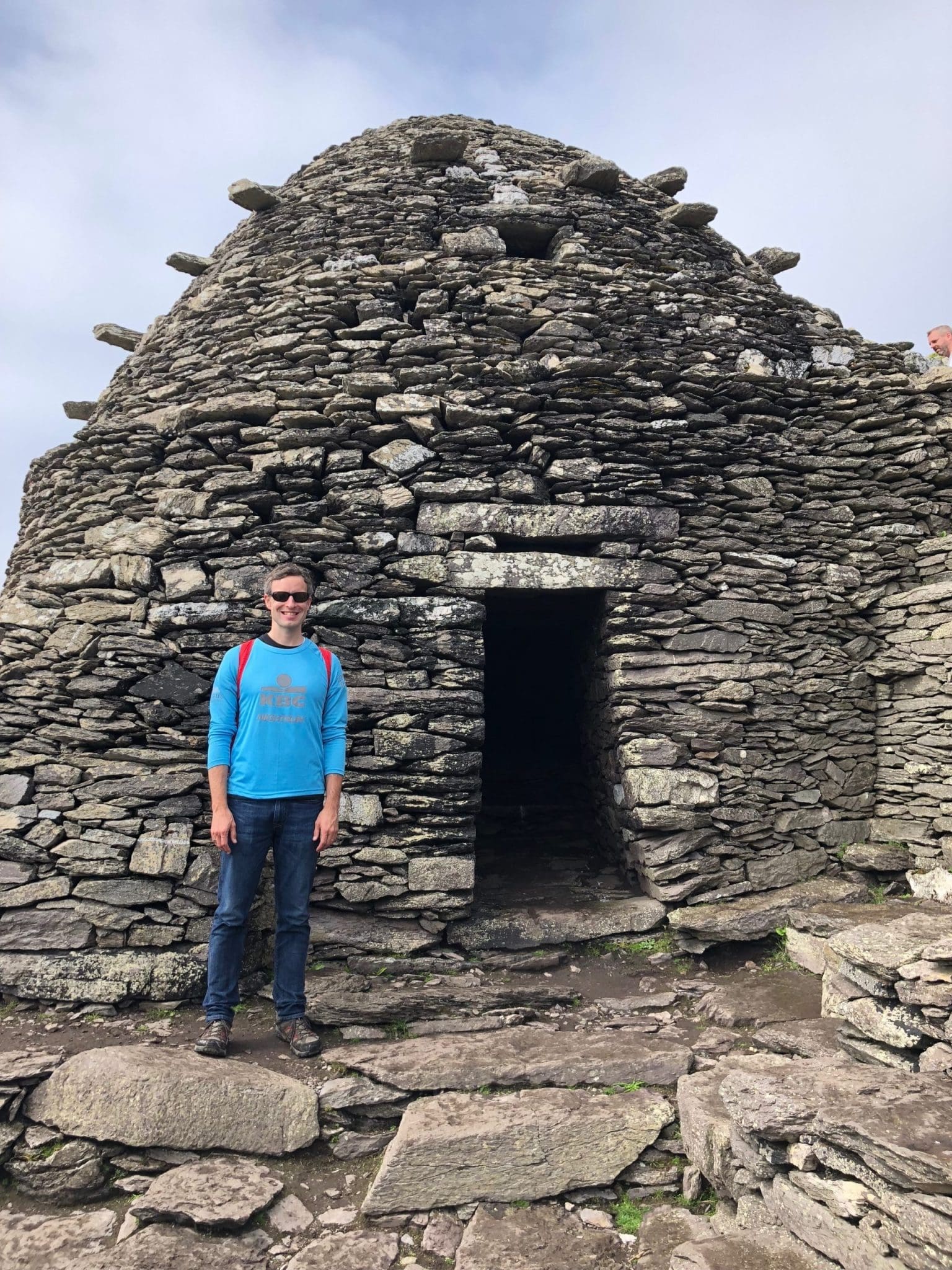 Man stands before a stone beehive hut on Skellig Michael, Ireland. Ancient monastic site.