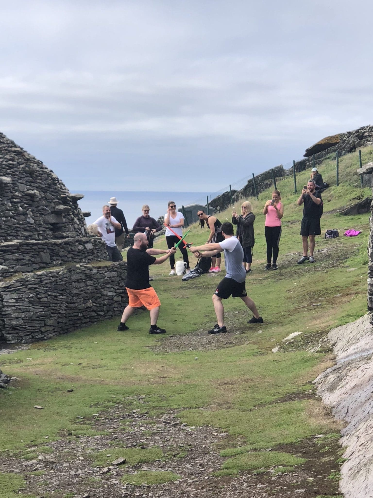 Men lightsaber dueling on Skellig Michael, Ireland. Tourists watch the fun.
