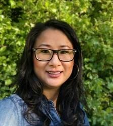 Woman with glasses smiling in front of green foliage
