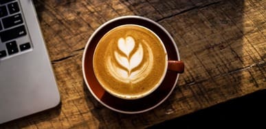 Latte art in a coffee cup next to a laptop in a downtown cafe.