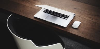 Laptop and mouse on wooden desk with modern chair. Minimalist workspace.