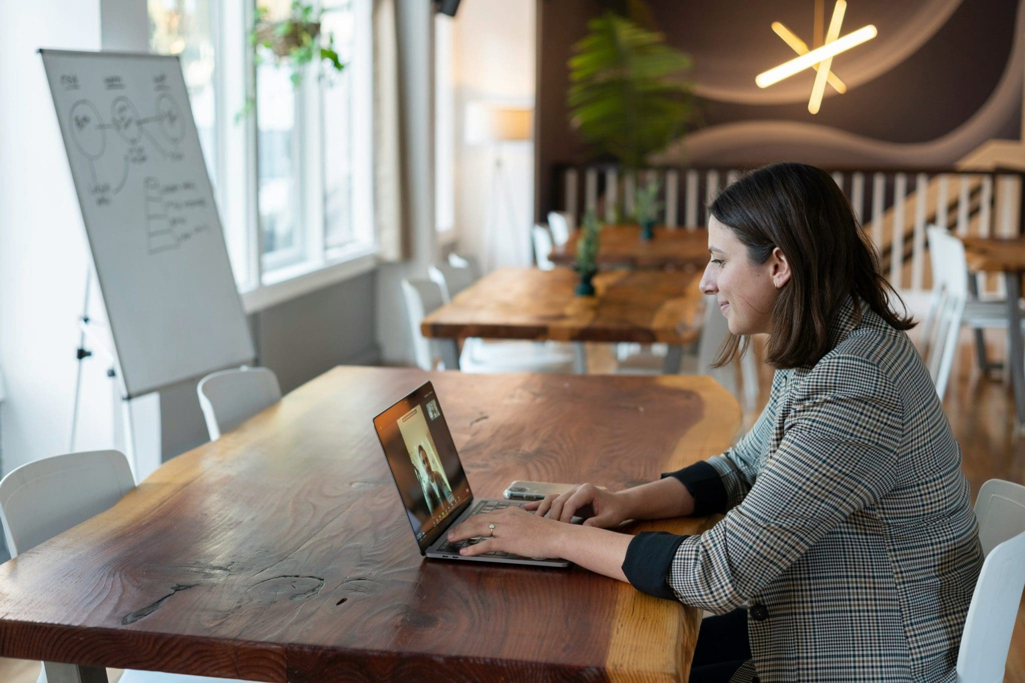 Woman on video call, possibly consulting, working on a laptop at a wooden table.