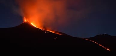 Mount Etna eruption at night with lava flowing down the volcano's side.