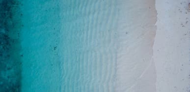 Aerial view of clear turquoise water meeting a white sand beach with subtle wave patterns.