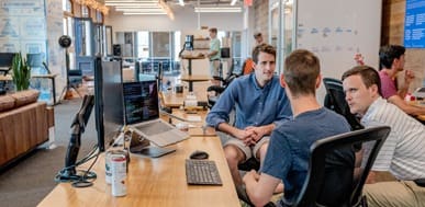 Office team collaborating, discussing project at desk with laptops and computers.