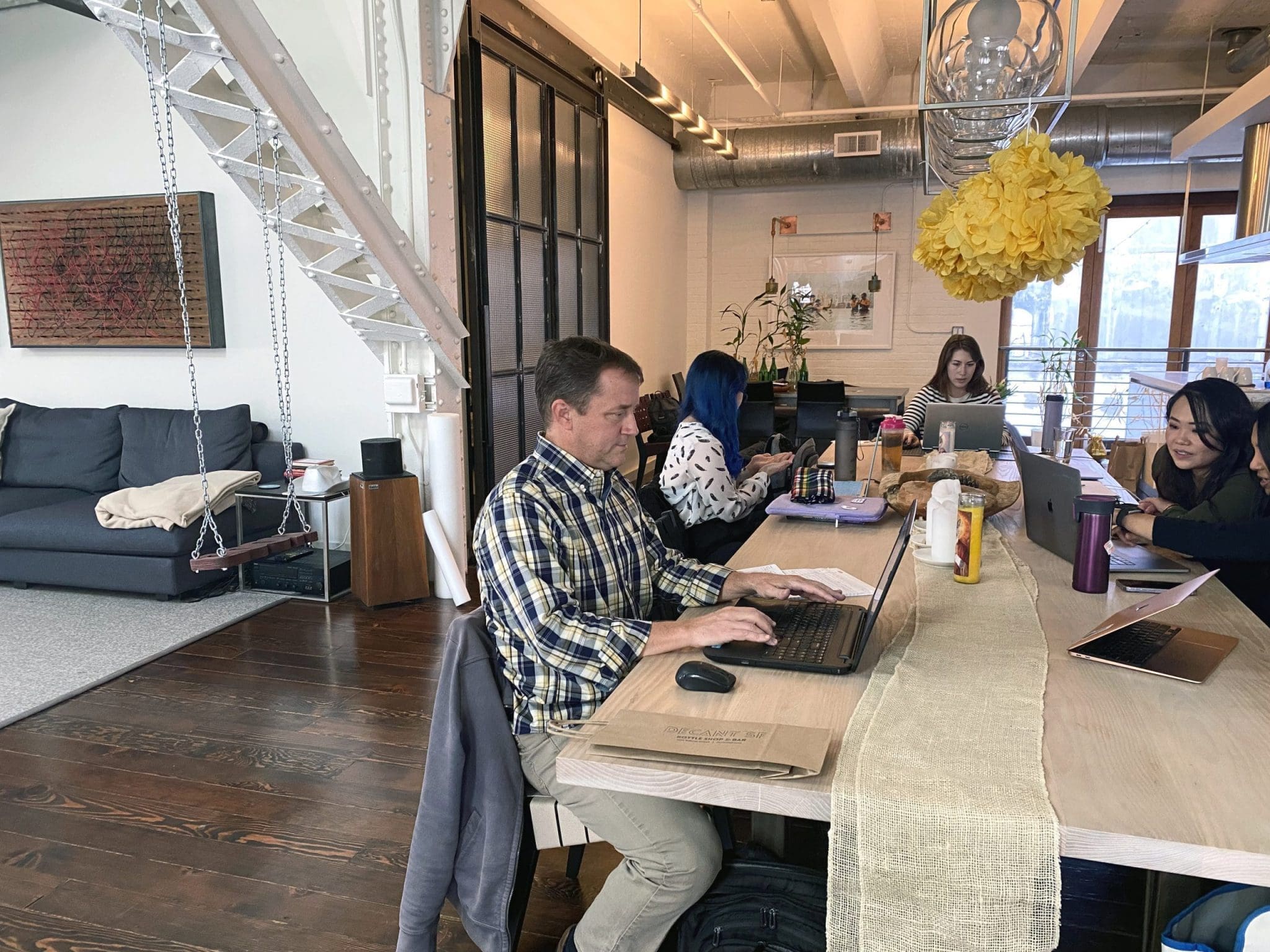 People working on laptops in a modern office with exposed beams and large windows.