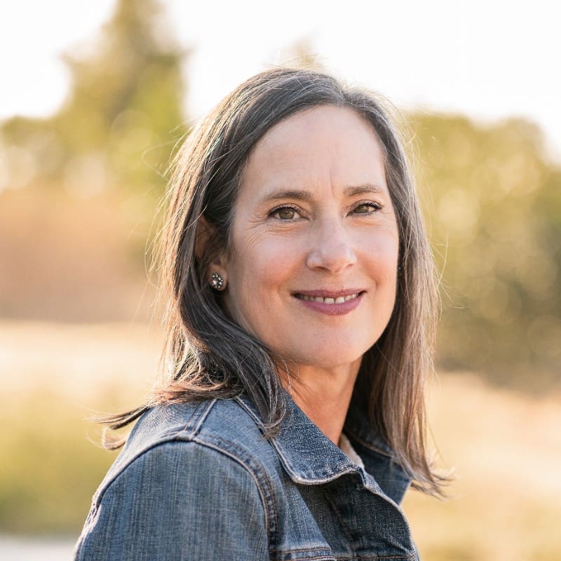 Woman with gray hair smiles in a denim jacket, outdoor portrait