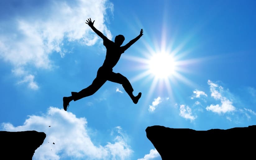 Silhouette of a person jumping between two cliffs against a sunny sky. Opportunity.