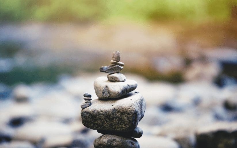 Balanced rock cairn near water, symbolizing sustained energy and burnout recovery.