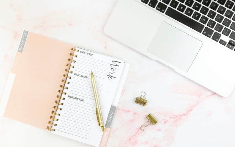 Work planner, laptop, and gold pen on a pink marble desk. "Work" section visible.