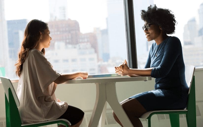 Two women networking at a table in a bright office setting.