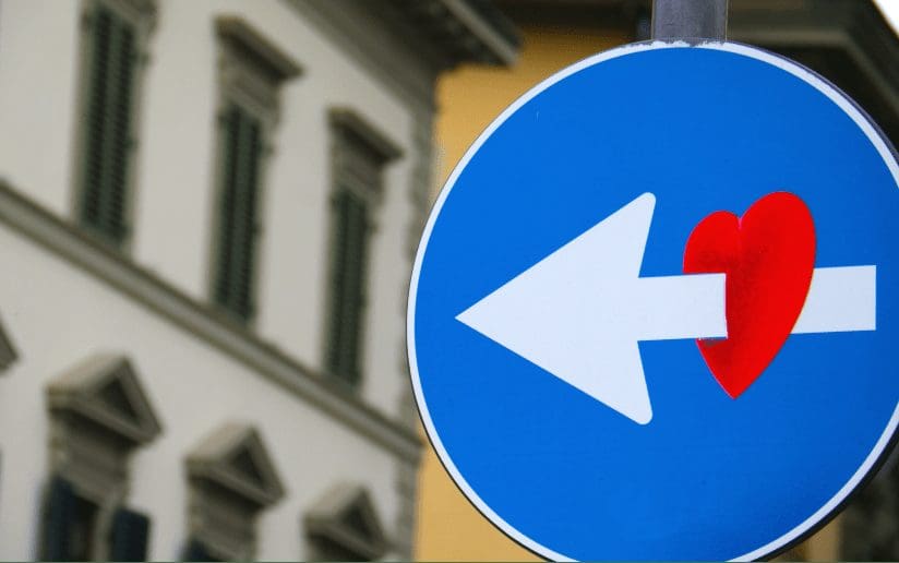 Street sign with a left arrow piercing a red heart, symbolizing tough love.