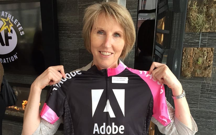 Woman holding an Adobe cycling jersey. The jersey is black and pink with the Adobe logo.