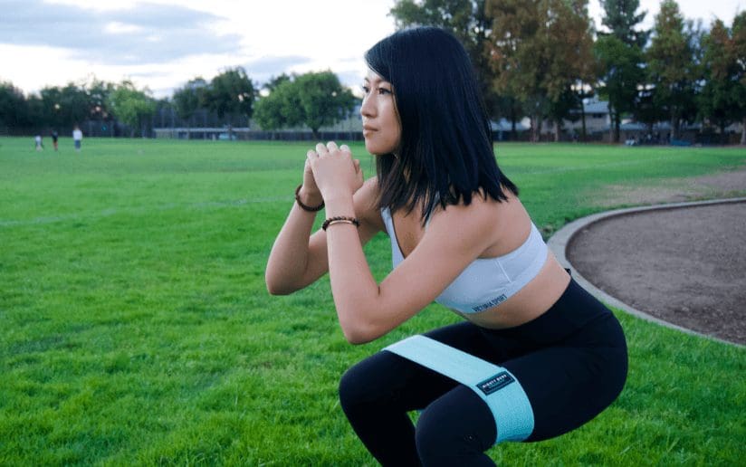 Woman doing squats with a resistance band on a grassy field. Powerlifting side hustle.
