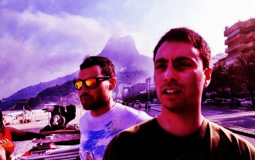 Two men on a beach with mountains in the background, possibly in Rio de Janeiro.