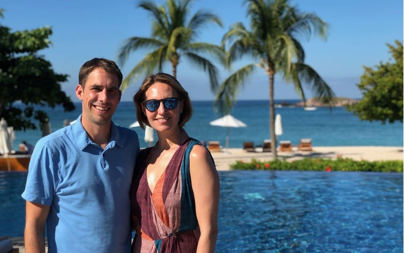 Couple posing by a pool with palm trees and ocean view in the background.