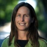 Woman smiling outdoors wearing a green jacket. Sustainable living advocate.