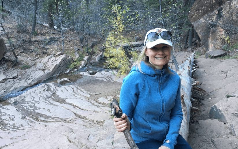 Gretchen Harding hiking in nature, smiling with a walking stick.