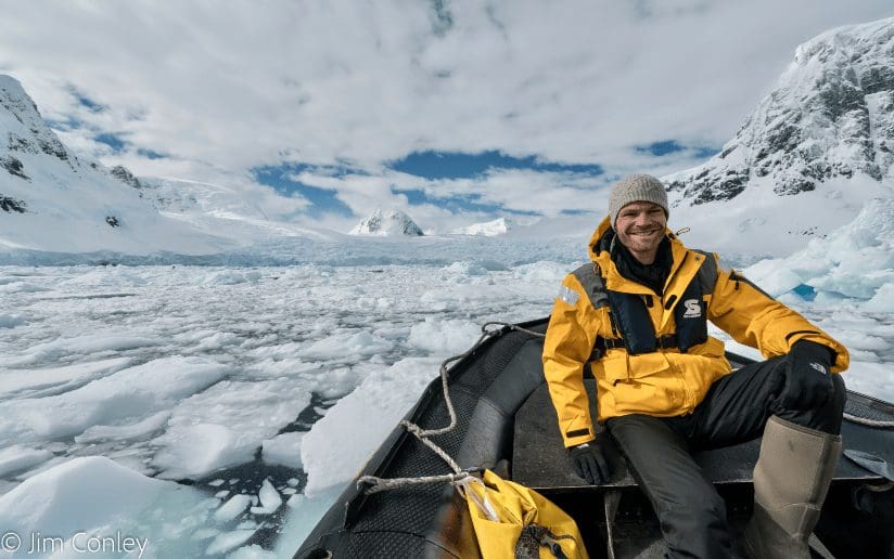 Jim Conley on a boat amidst ice floes in Antarctica, wearing a yellow jacket.