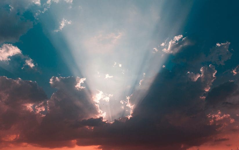 Sun rays beaming through clouds in a teal and red sky
