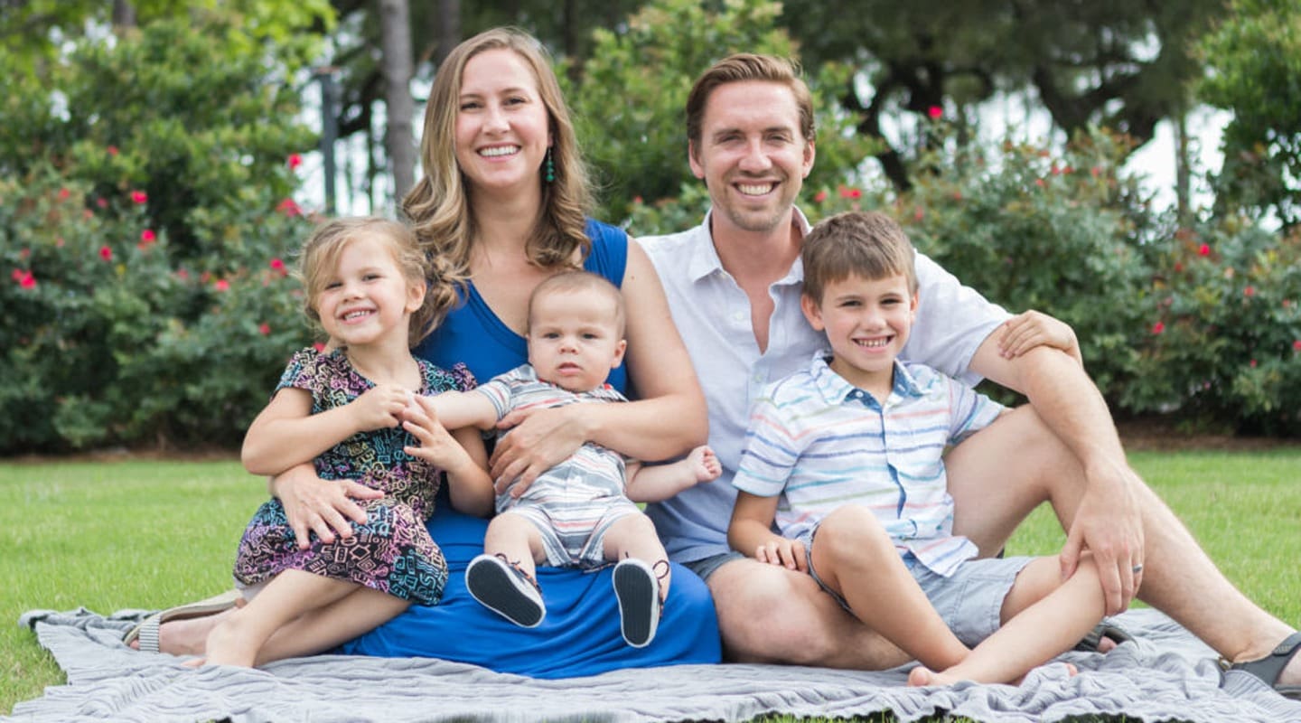 Family of five smiling together outdoors, featuring a mother, father, and three children.