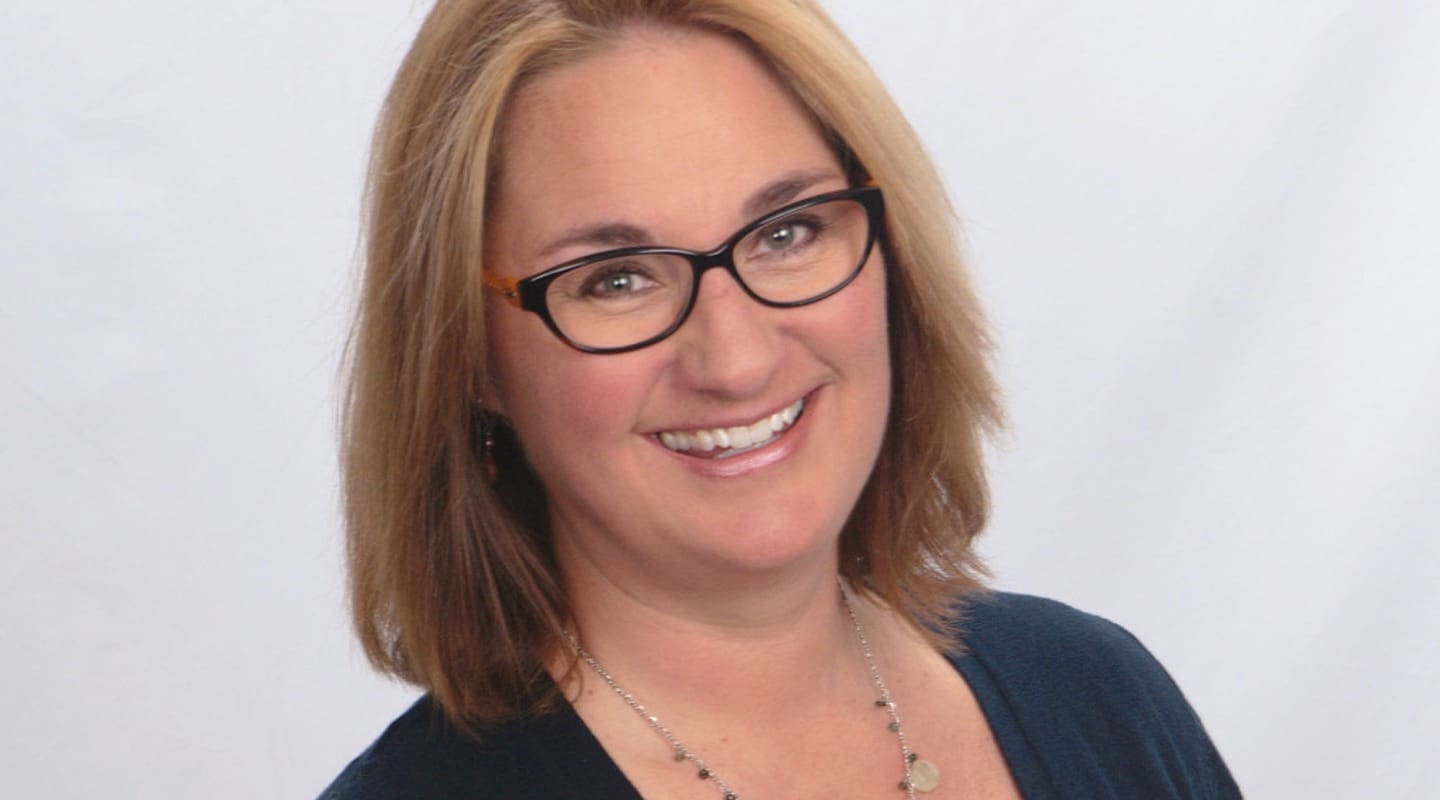 Ali Ward, smiling, wearing glasses and a necklace