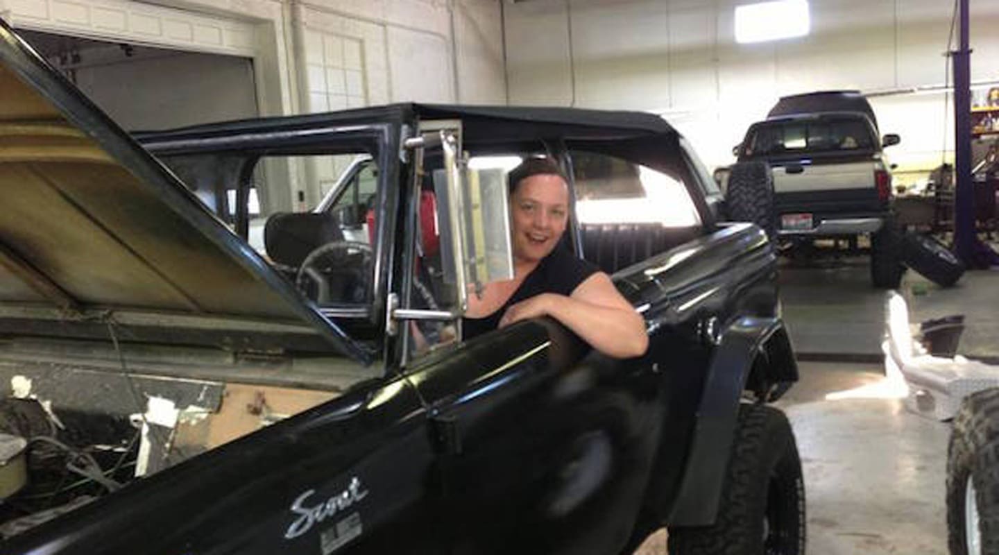 Audrey Tracy smiles from a black vintage Scout SUV with the hood open in a garage setting.