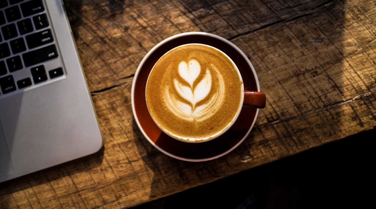 Latte art coffee with laptop on rustic wooden table