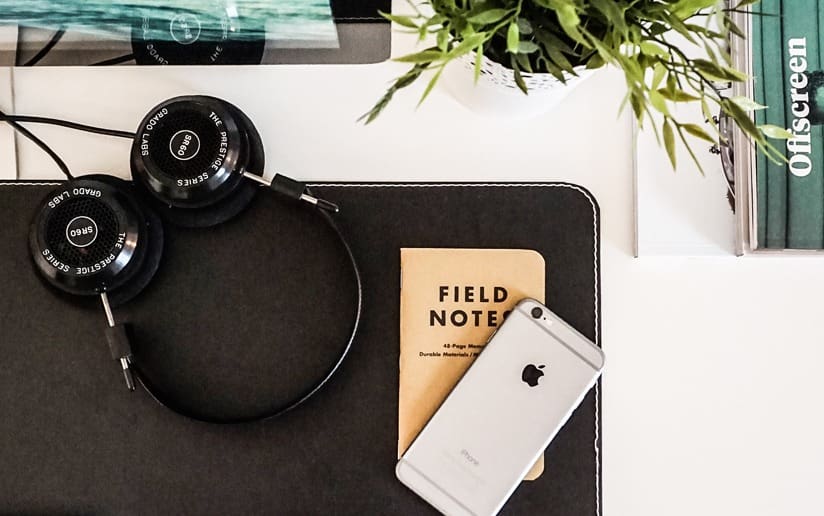 Grado SR60 headphones, Field Notes notebook, and iPhone on a desk. Offscreen magazine visible.