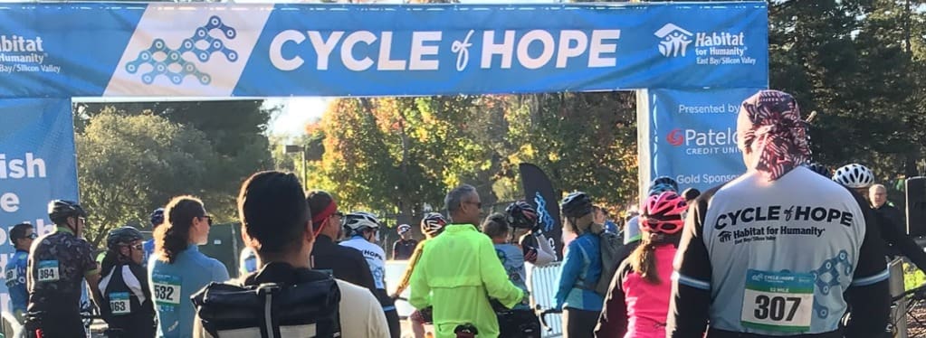 Cyclists at the Cycle of Hope event for Habitat for Humanity, passing under the event banner.