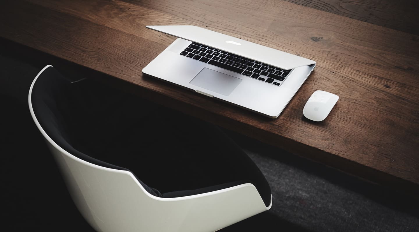 Laptop and mouse on a wooden desk, next to a modern chair; consulting business setup.