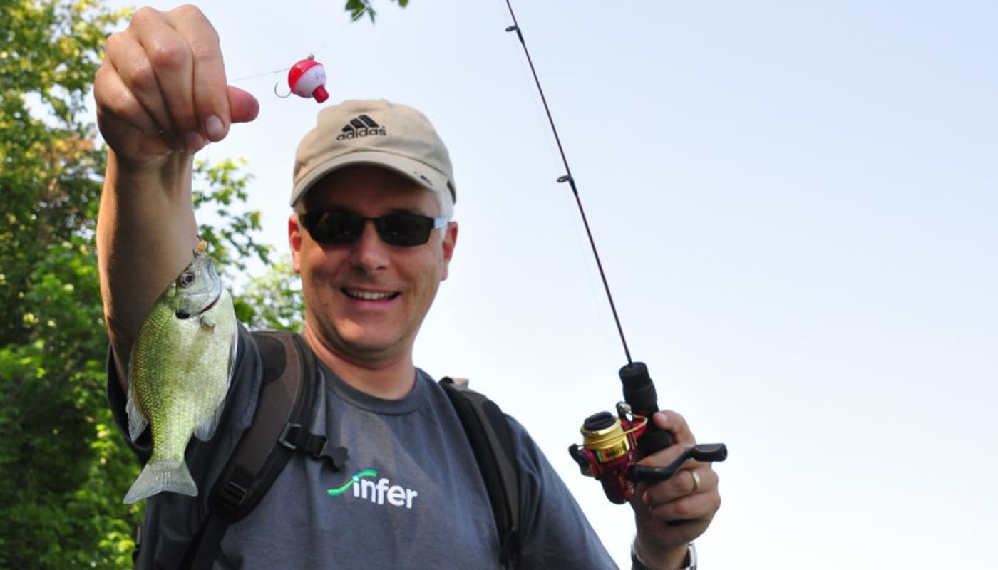 Jim Herbold fishing, holding a small fish, with a fishing rod and bobber.