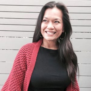Woman with long dark hair smiles while wearing a red cardigan and black shirt.