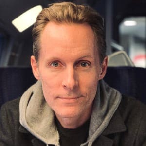 Man with light brown hair wearing a gray hoodie, looking at the camera