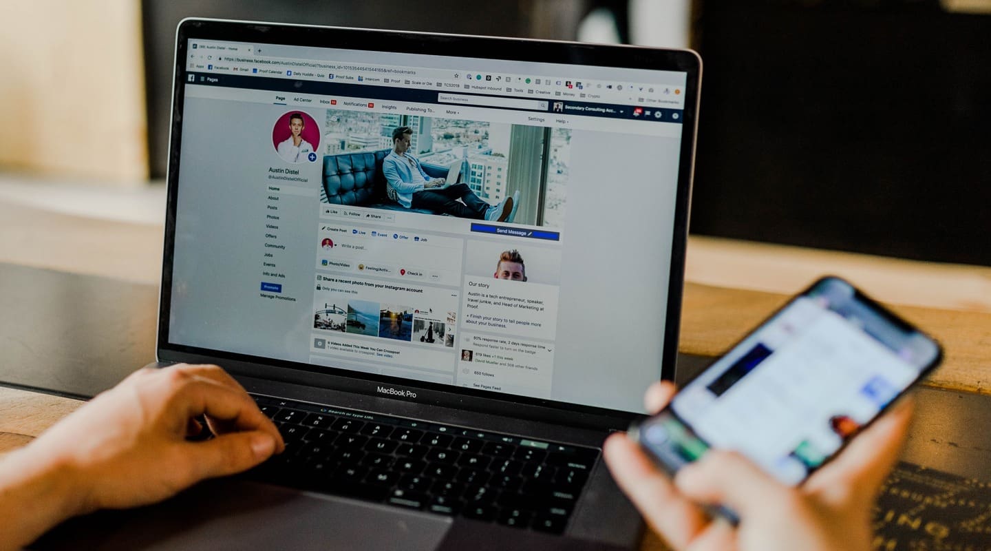 Person using MacBook Pro and iPhone, likely managing social media. Proof Marketing.