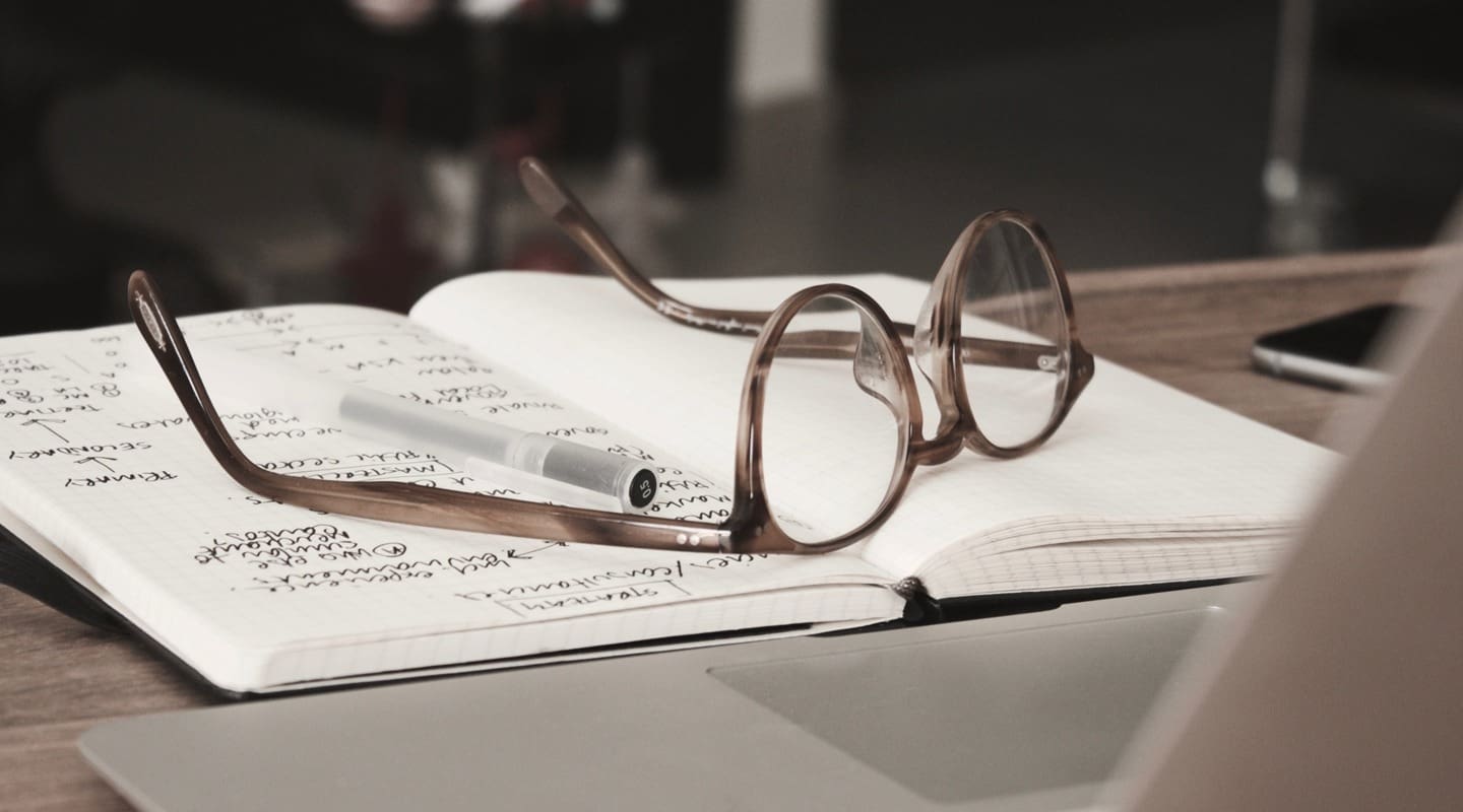 Notebook with handwritten strategy notes, glasses, pen, and laptop, ideal for consultant work.