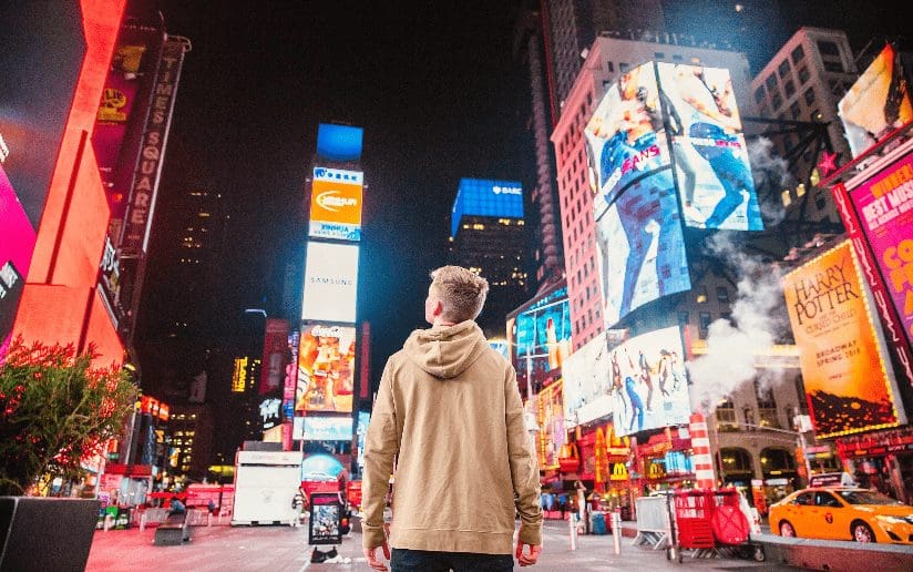 Man looking at bright billboards in Times Square, NYC. Future of Brands Post-Pandemic.