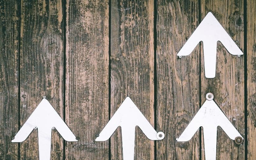 White arrows pointing up on a rustic wooden background, symbolizing growth for B2B blog promotion.