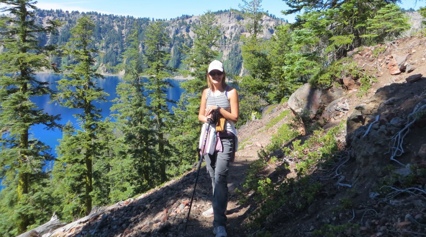 Woman hiking near Crater Lake, wearing a hat and using trekking poles; stunning blue water view