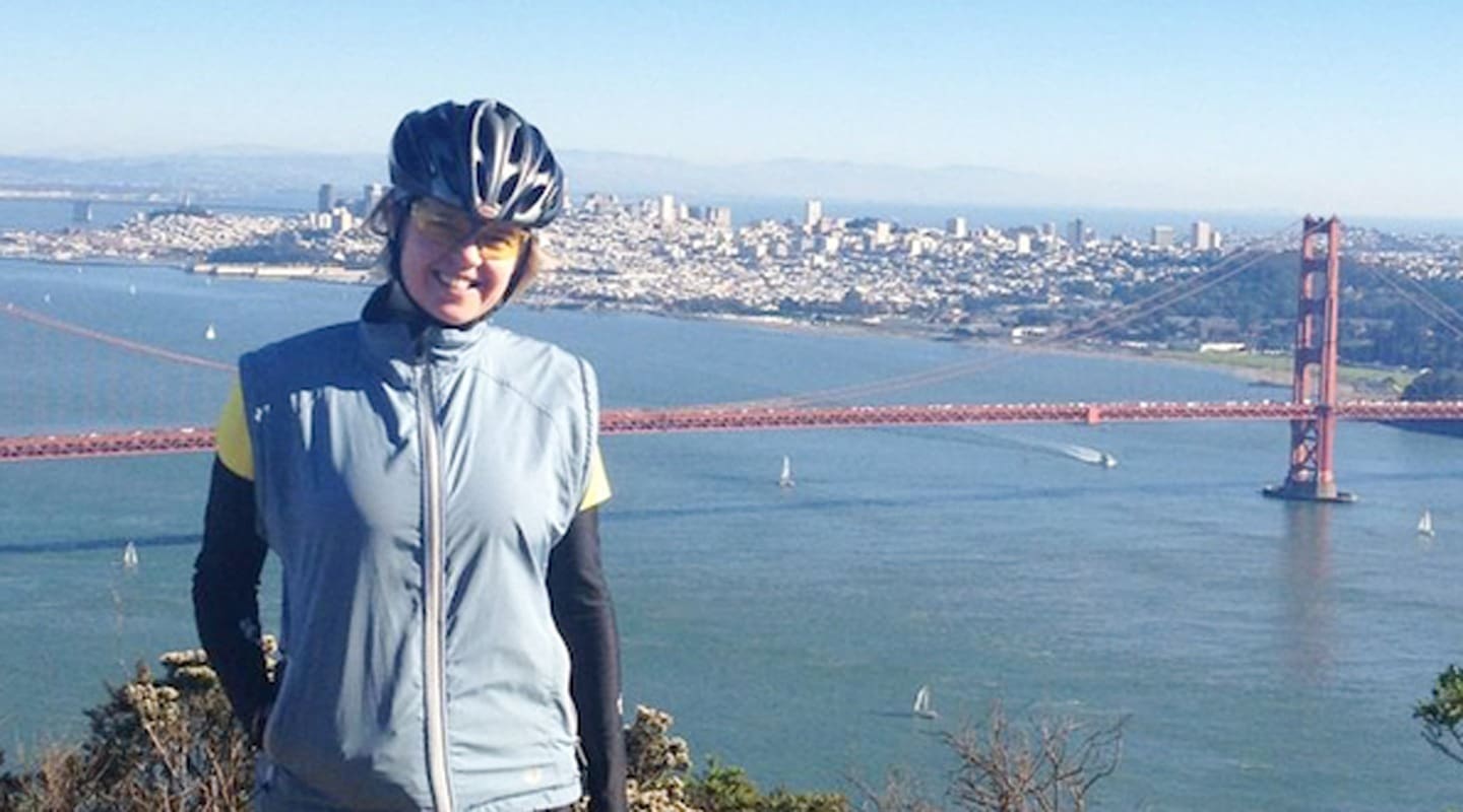 Ruta Jaks smiles in cycling gear with the Golden Gate Bridge and San Francisco skyline behind her.
