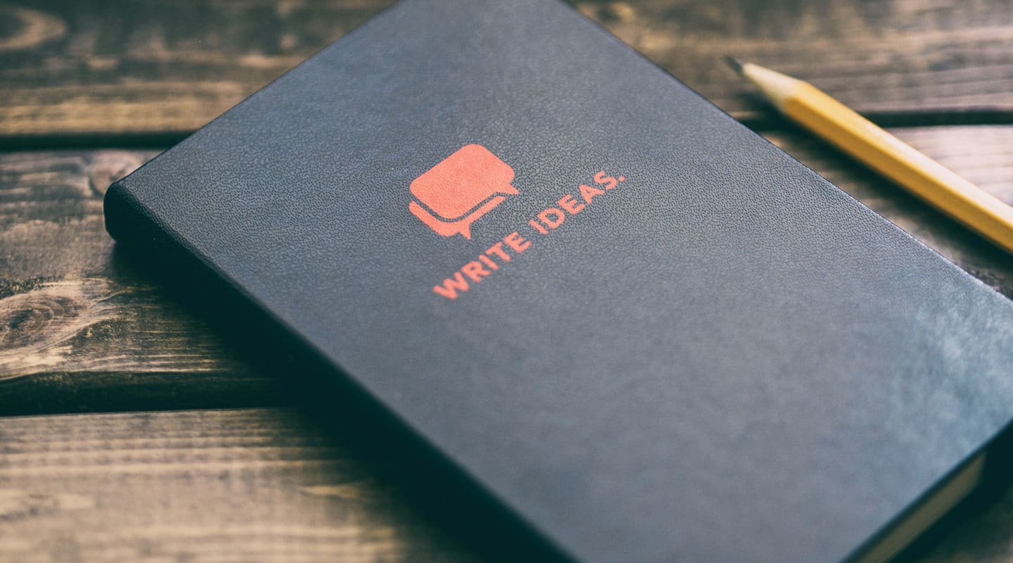 Black notebook with WRITE IDEAS printed on cover, next to a pencil, perfect for story ideas.