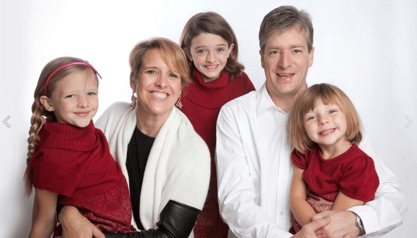 Family portrait: mother, father, and three daughters smiling in red and white.