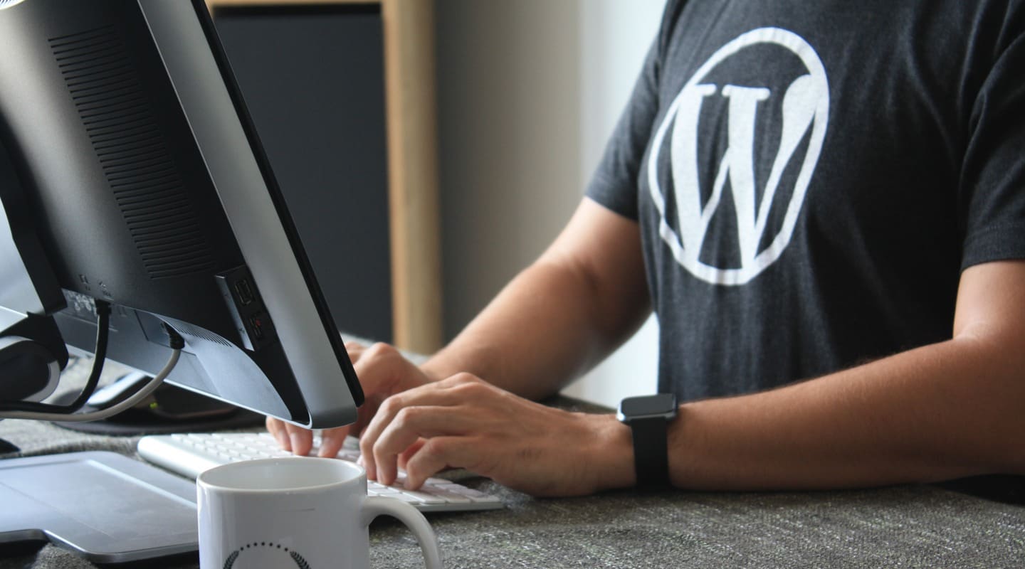 Man working on a computer, wearing a WordPress t-shirt and using a keyboard.