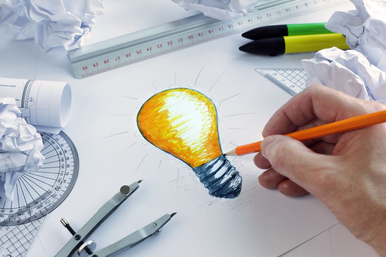Hand sketching a lightbulb, symbolizing creative ideas and innovation on a design table.