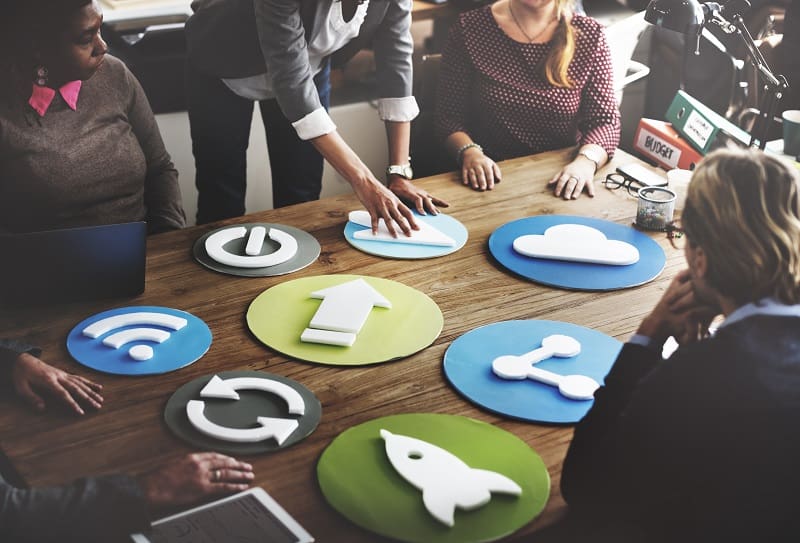 Marketing team brainstorming around social media and digital marketing icons on a wooden table.