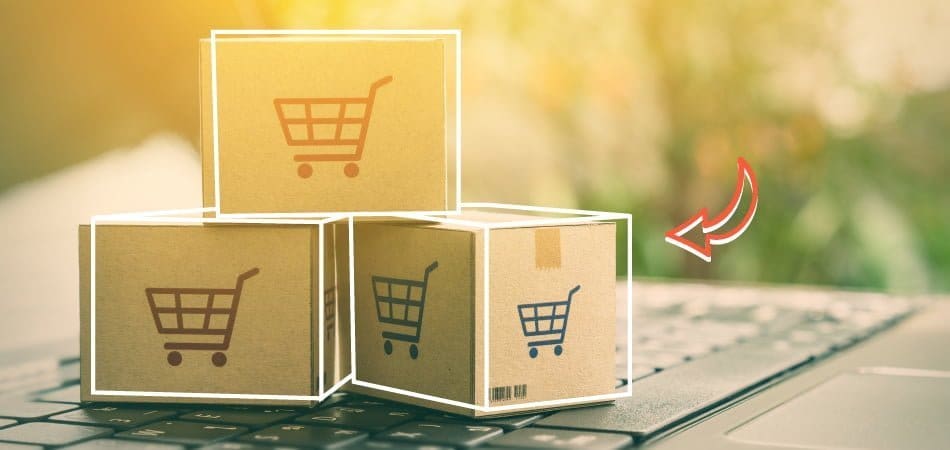 Cardboard boxes with shopping cart icons representing e-commerce shipping and delivery on a laptop keyboard.