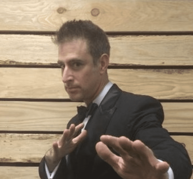 Man in tuxedo poses with martial arts stance, ready to demonstrate.
