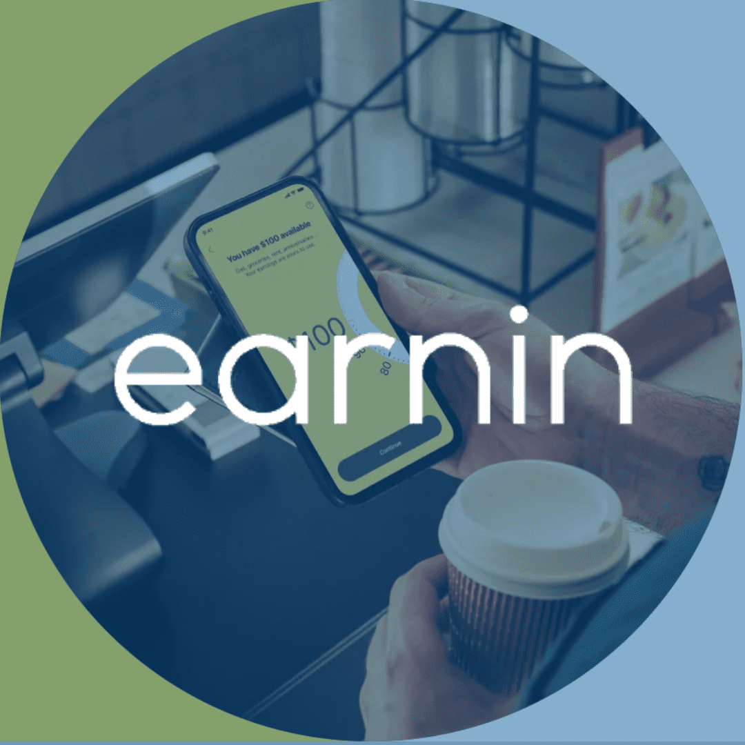 Person using the Earnin app on their phone, showing $100 available. Holding a coffee cup at a checkout.